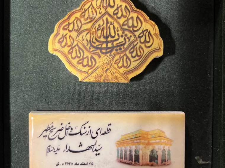 قطعه‌ای مذهّب از سنگ ضریح در جعبه‌ی مخملی سبز، همراه پلاک مرمرین با تصویر حرم